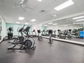 A gym with a variety of exercise equipment including treadmills, stationary bikes, and elliptical machines.